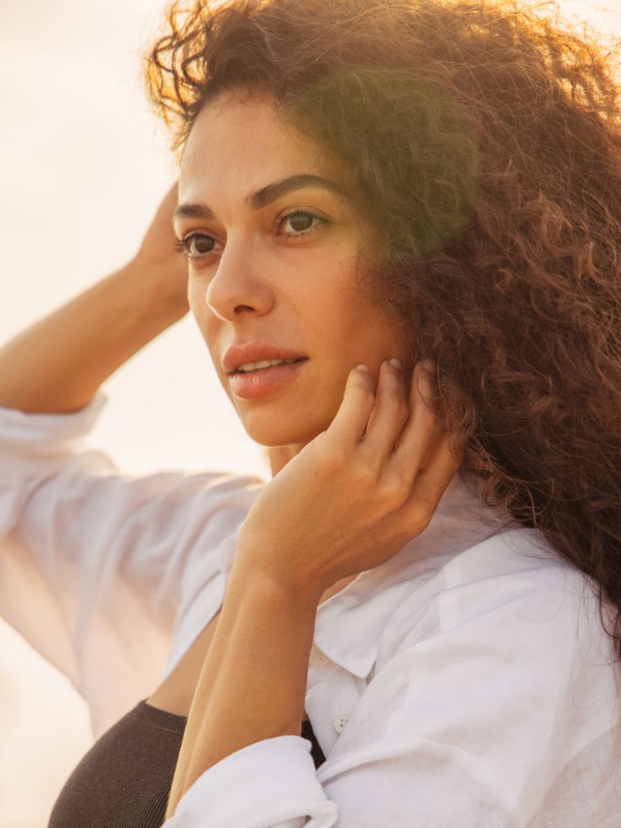 Woman with long brown curly hair backlit, golden hour